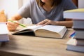 Top view and selective focus shot of woman who is reading textbook on table with stacks of many books as foreground shows