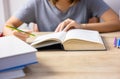 Top view and selective focus shot of woman who is reading textbook on table with stacks of many books as foreground shows