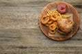 Top view of serving board with tasty burger, French fries and fried onion rings on wooden table, space for text. Fast food Royalty Free Stock Photo