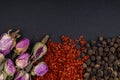 Top view of a set of spices and herbs tea rose buds red chili pepper flakes and black peppercorns on black background Royalty Free Stock Photo