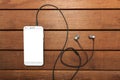 A top view of a set of wired earbud headphones and mobile phone blank template lying on a rustic wooden table. mockup image Royalty Free Stock Photo