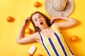 Top view of shocked surprised cheerful young woman wearing striped swimsuit lies isolated on yellow background posing surrounded