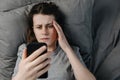 Top view of shocked young woman reads terrifying news in morning lying on pillow in bed looking, stares at smart phone device