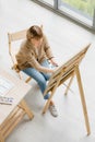 Top view shot of Caucasian old senior elderly retired female painter sitting on wooden chair using watercolor paintbrush and Royalty Free Stock Photo