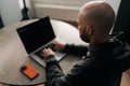 Top view from shoulder of young bald programmer with beard and ear piercing sitting at table in home office Royalty Free Stock Photo