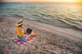 Top view of slender young caucasian woman in hat works on his laptop resting on sandy beach on sunset. Slender legs and Royalty Free Stock Photo