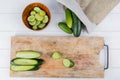 top view of sliced and cut cucumber on cutting board with bowl of cucumber slices and cucumbers spilling out of sack on wooden