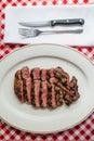 Top view of Sliced medium rare charcoal grilled wagyu Ribeye steak in white plate on red and white pattern tablecloth with cutlery