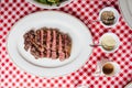 Top view of Sliced medium rare charcoal grilled wagyu Ribeye steak in white plate on red and white pattern tablecloth.