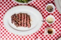 Top view of Sliced medium rare charcoal grilled wagyu Ribeye steak in white plate on red and white pattern tablecloth.