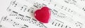 Top view of small red heart on paper sheet with musical notes close-up. Royalty Free Stock Photo