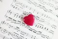 Top view of small red heart on paper sheet with musical notes close-up. Royalty Free Stock Photo