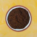 Top view of a small terracotta spice bowl filled with chili powder on a yellow painted tabletop