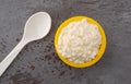 Top view of a small yellow bowl of pineapple cottage cheese with a spoon to the side on a gray table