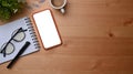 Top view smart phone, coffee cup and notepad on wooden desk.