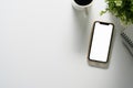 Top view smartphone with blank screen, coffee cup, notepad and house plant on white table, copy space Royalty Free Stock Photo