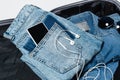 top view of smartphone in pocket of jeans near earphones, denim shirt and sunglasses packed in travel bag.