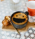 Top view smile face creama on hot black coffee in black ceramic cup on wooden tray put white table with red plastic cups and glass Royalty Free Stock Photo