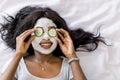 Top-view of smiling African woman making spa procedures with mud facial mask and fresh cucumber slices on eyes, laying Royalty Free Stock Photo