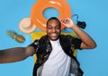 Top view of smiling black guy in summertime outfit lying on lilo, taking selfie on beach vacation, blue background