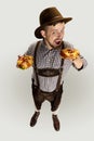 High angle view of smiling man, waiter in traditional Bavarian costume with yummy pretzels isolated over grey background