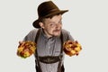 High angle view of smiling man, waiter in traditional Bavarian costume with yummy pretzels isolated over grey background