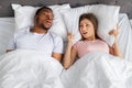 Top view of snoring black guy and his frustrated girlfriend covering ears with pillow in bed at home Royalty Free Stock Photo