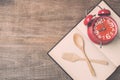 Top view spoon, fork, book and red clock on wooden plank background