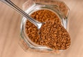 Top view on spoon with instant granulated coffee over a jar on a wooden background.