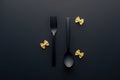 Top view of spoon upside down and fork near farfalle pasta on black background. Royalty Free Stock Photo