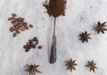 Spoonful of coffee, star anise seeds, and coffee beans on white surface