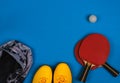 Top view on the sport composition with sneakers, jacket, tennis rocket with ball on the bright blue background