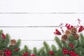 Top view of spruce branches, pine cones, red berries and bell on white wooden table background. Royalty Free Stock Photo