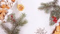 Top view of the spruce branches and unpacked christmas present with sweets on a white textured surface.