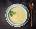 Top view of squash cream soup with parsley leaves in a bowl on a plate. Wooden spoon on a dark surface