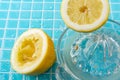 Top view of squeezed lemon, with glass juicer and lemon juice, on light blue ceramic with water drops, selective focus