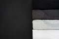 Top view stack of black, grey and white monochrome t-shirt rolled up on black background, copy space, flat lay