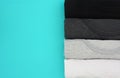 Top view stack of black, grey and white monochrome t-shirt rolled up on blue background, copy space, flat lay