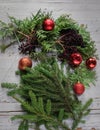 Top view of stages of making Christmas wreath with fir branches and decorative red balls on wooden rustic tabletop