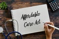 Top view of stethoscope,calculator,plant and hand writing Affordable Care Act on notebook on wooden background