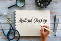 Top view of stethoscope,magnifying glass,clock,pen and hand holding pen writing Medical Checkup on notebook on wooden background Royalty Free Stock Photo