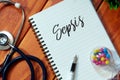 Top view of stethoscope,pen and notebook written with Sepsis on wooden background. Health concept.