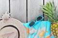 straw hat, beach towel, sunglasses and pineapple on wooden terrace