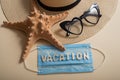 Top view of straw hat sunglasses starfish and mask with lettering vacation. Travel concept during the spread of