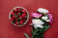 Top view of strawberries in bowl on red background bouquet of peonies Royalty Free Stock Photo