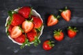 Strawberries in a bowl showing fresh ripe whole and cut in half strawberry fruits in a white bowl on dark background Royalty Free Stock Photo