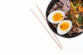 Top view studio shot of black bowl of ramen noodles with boiled eggs, veggies and turkey meet, ready to be poured with