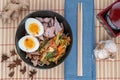 Top view studio shot of black bowl of ramen noodles with boiled eggs, veggies and turkey meet, ready to be poured with