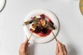 Top view stuffed fish on a white plate. Hands of a girl with gilded appliances.