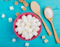 top view of sugar cubes in a pink bowl and wooden spoons with sugar on blue background Royalty Free Stock Photo